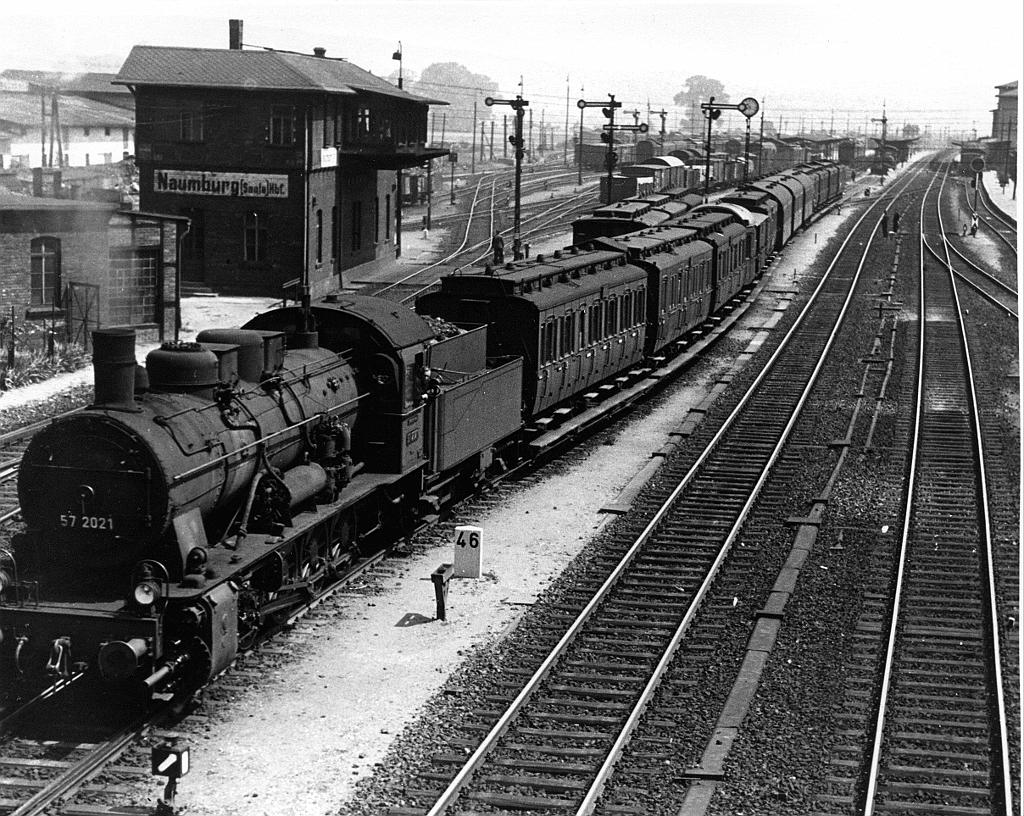 57_2021_Naumburg Zugausfahrt1.jpg - 57 2021 verläßt einer bunten Garnitur von Personenwagen den Bahnhof Naumburg in Richtung Weimar. Der Fotostandort ist heute noch vorhanden, die Straßenbrücke mit der Straße ins Unstruttal nach Freiburg. Ansonsten wird man den Bahnhof kaum wiedererkennen. Die Formsignale sind gegen Lichtsignale ausgetauscht worden. Das Stellwerk und das Bw links werden lage nicht mehr genutzt bzw. sich auch schon nicht mehr vorhanden. Der Fahrdienstleiter hat heute sein Sitz in Leipzig dank ESTW (Elektronisches Stellwerk). Die Bahnsteige sind komplett erneuert worden für den ICE-Verkehr. Die Aufnahme hat mein Vater Gerhard Hechler  wohl nach 1936, den Olympischen Spielen in Deutschland, gemacht.